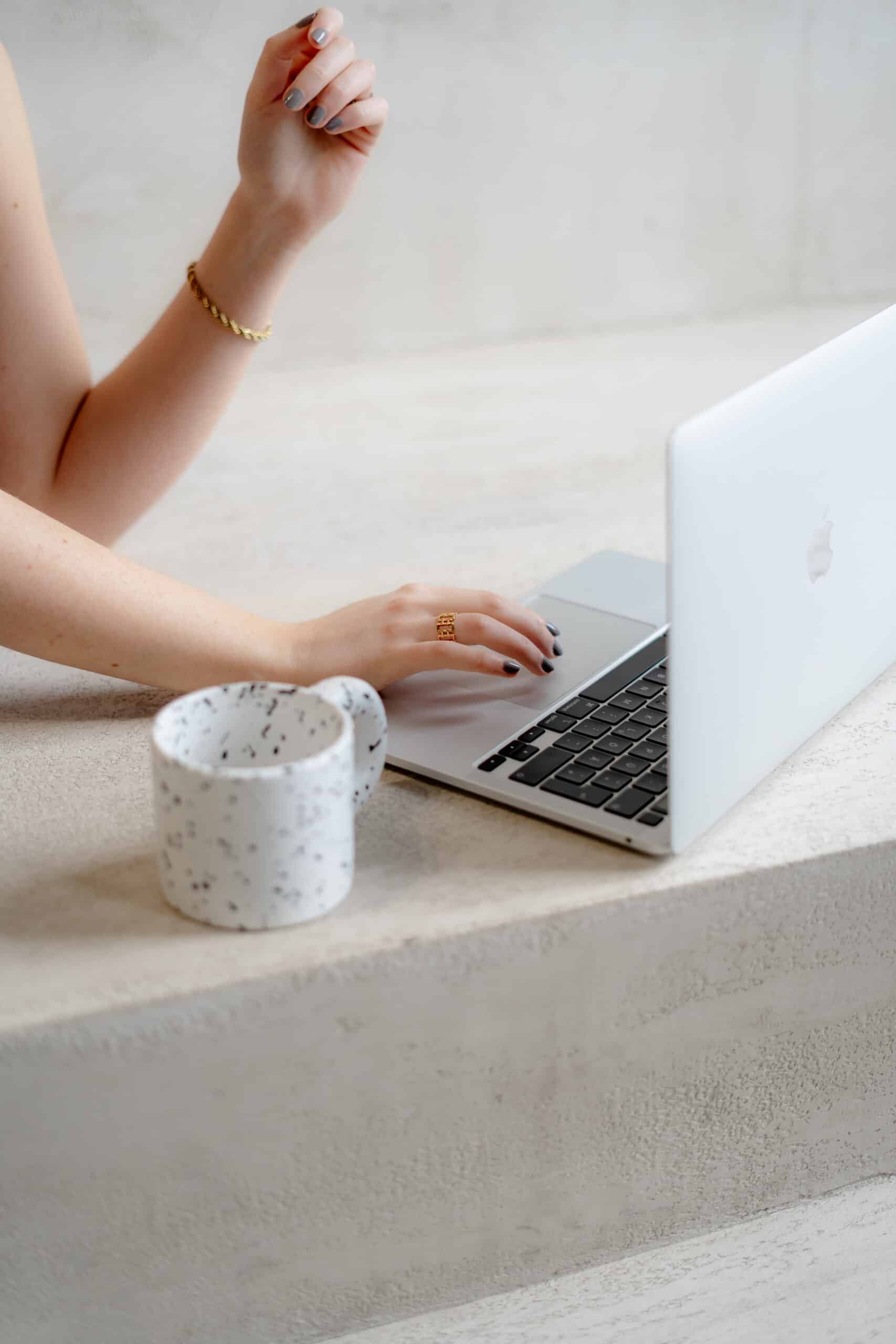 Eine Hand tippt auf einem Macbook neben einer Tasse Kaffee – symbolisch für die kreative und professionelle Arbeit von Kristina Webdesigns, einer Webdesign-Agentur in der Region Hamburg, die moderne und maßgeschneiderte Websites für Unternehmen entwickelt.